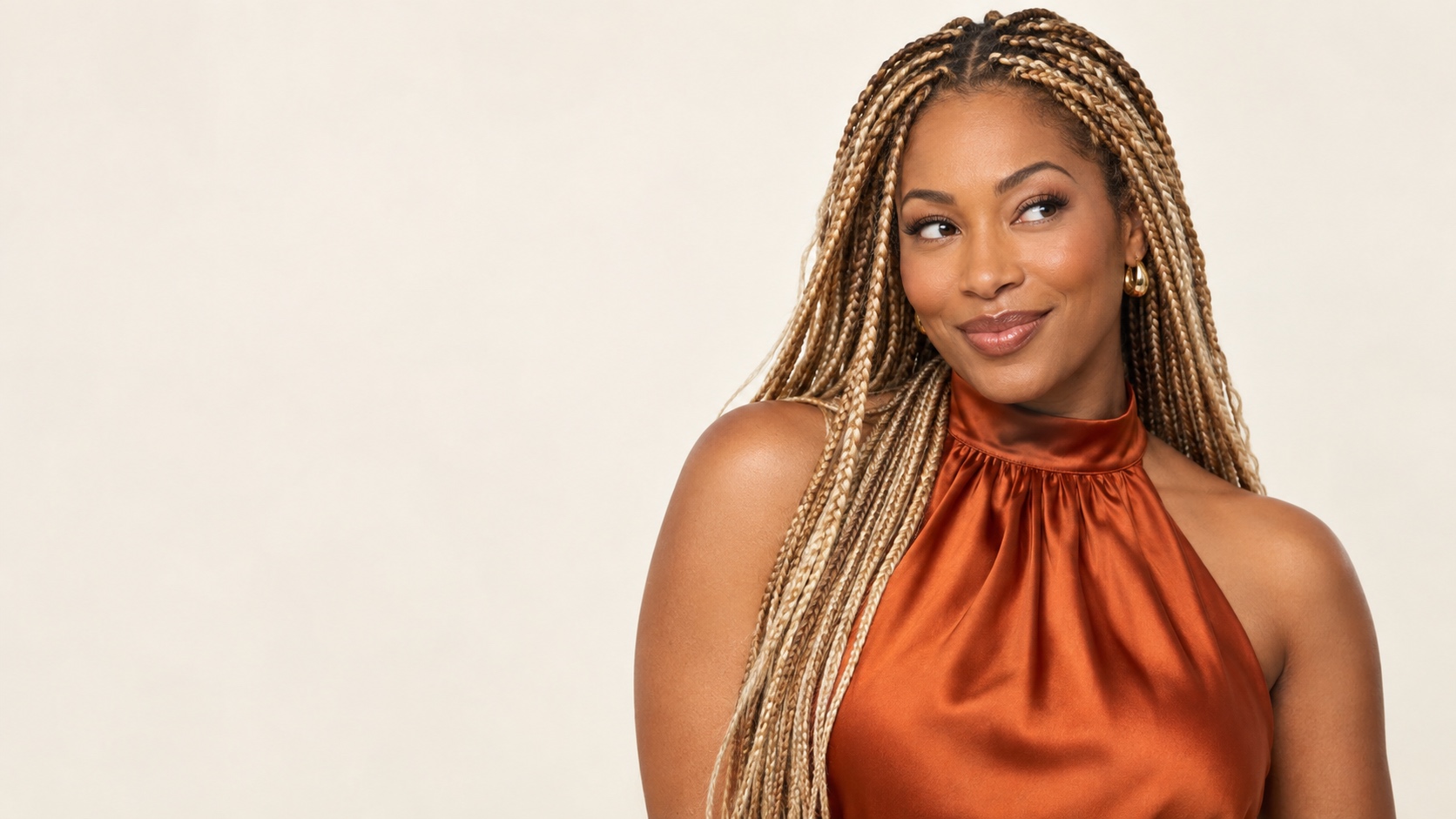 Woman in a rust satin top with long hot-honey-blonde box braids looking to the side