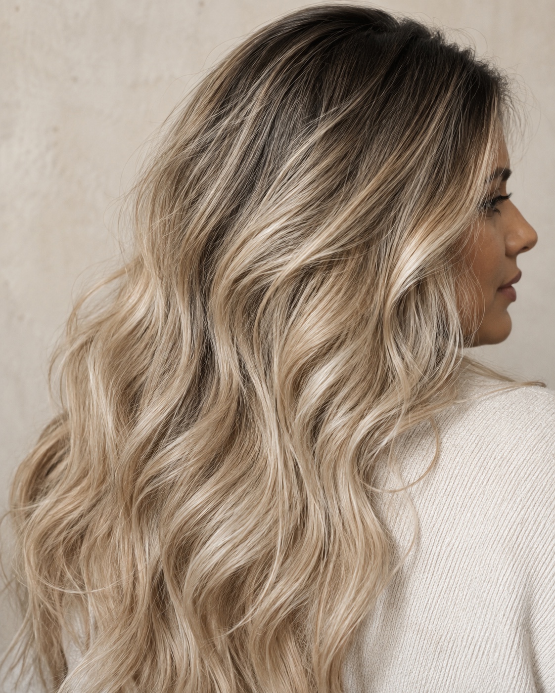Close-up of neutral oat-milk-blonde waves with a soft dark root melt and creamy beige ribbons